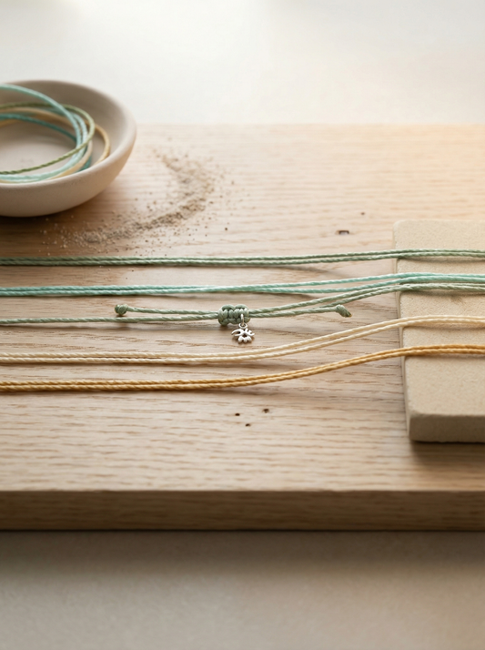 Waxed polyester cords horizontally on pale oak with bisque dish, sandstone, and sifted sand.
