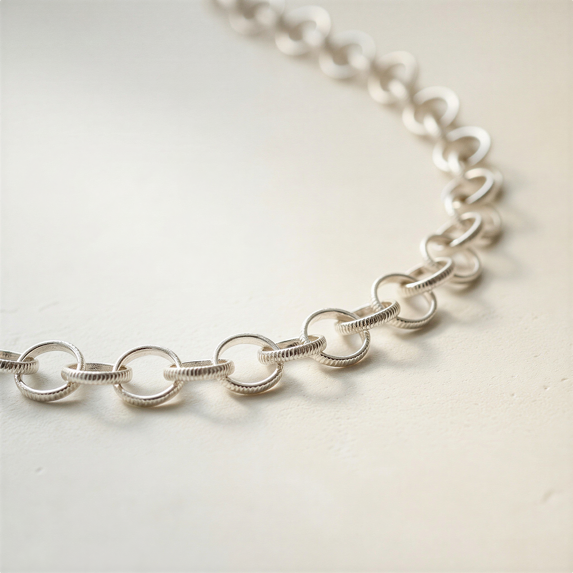 Textured sterling silver rolo chain with 2x10mm links photographed on neutral surface with enhanced clarity, true color, soft highlights