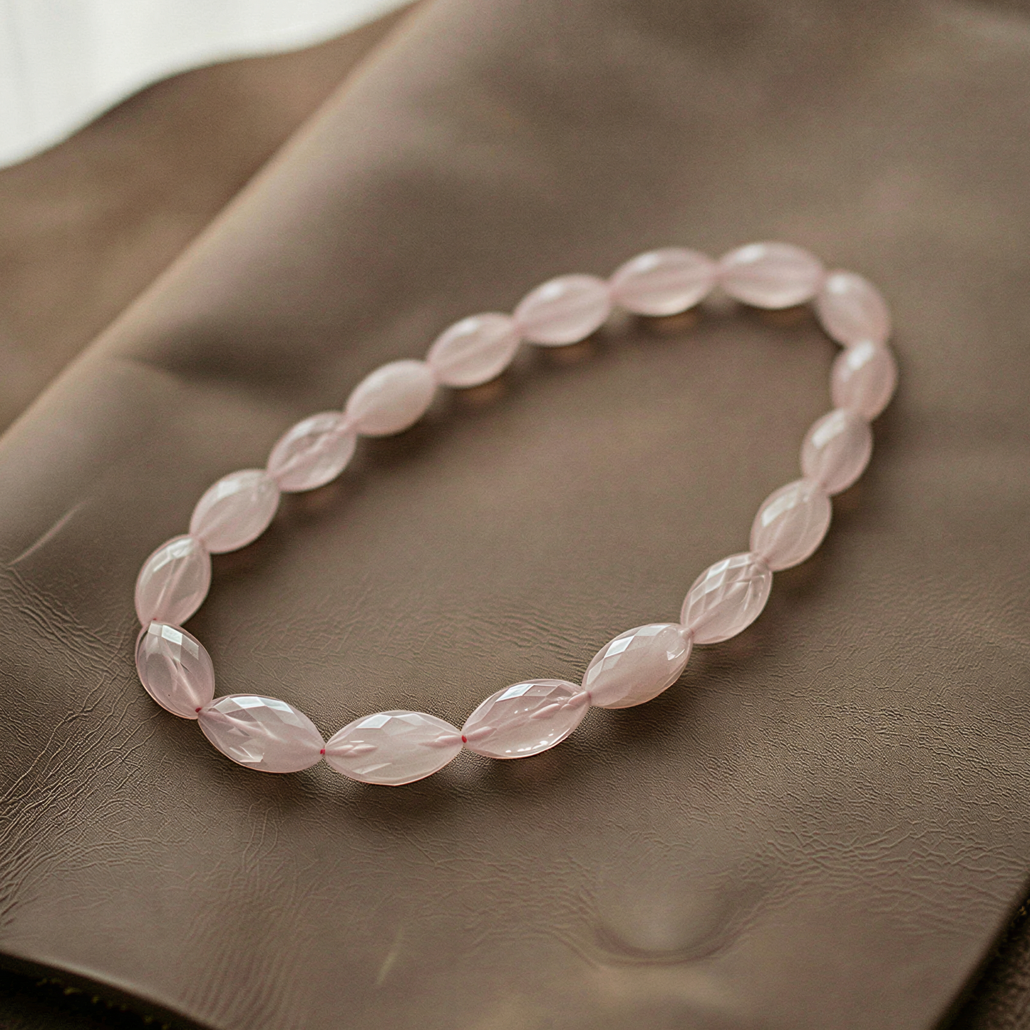Faceted rose quartz marquise beads forming a seamless circular strand, softly glowing on textured fabric with gentle highlights and delicate shadows.