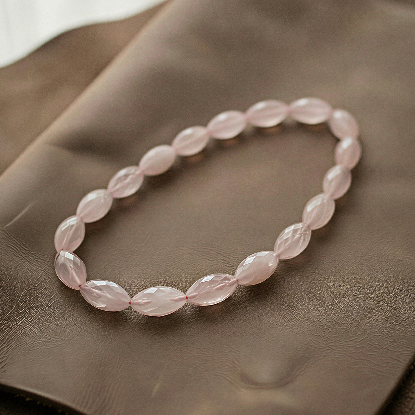 Faceted rose quartz marquise beads forming a seamless circular strand, softly glowing on textured fabric with gentle highlights and delicate shadows.