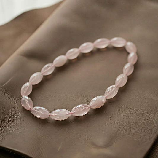 Faceted rose quartz marquise beads forming a seamless circular strand, softly glowing on textured fabric with gentle highlights and delicate shadows.