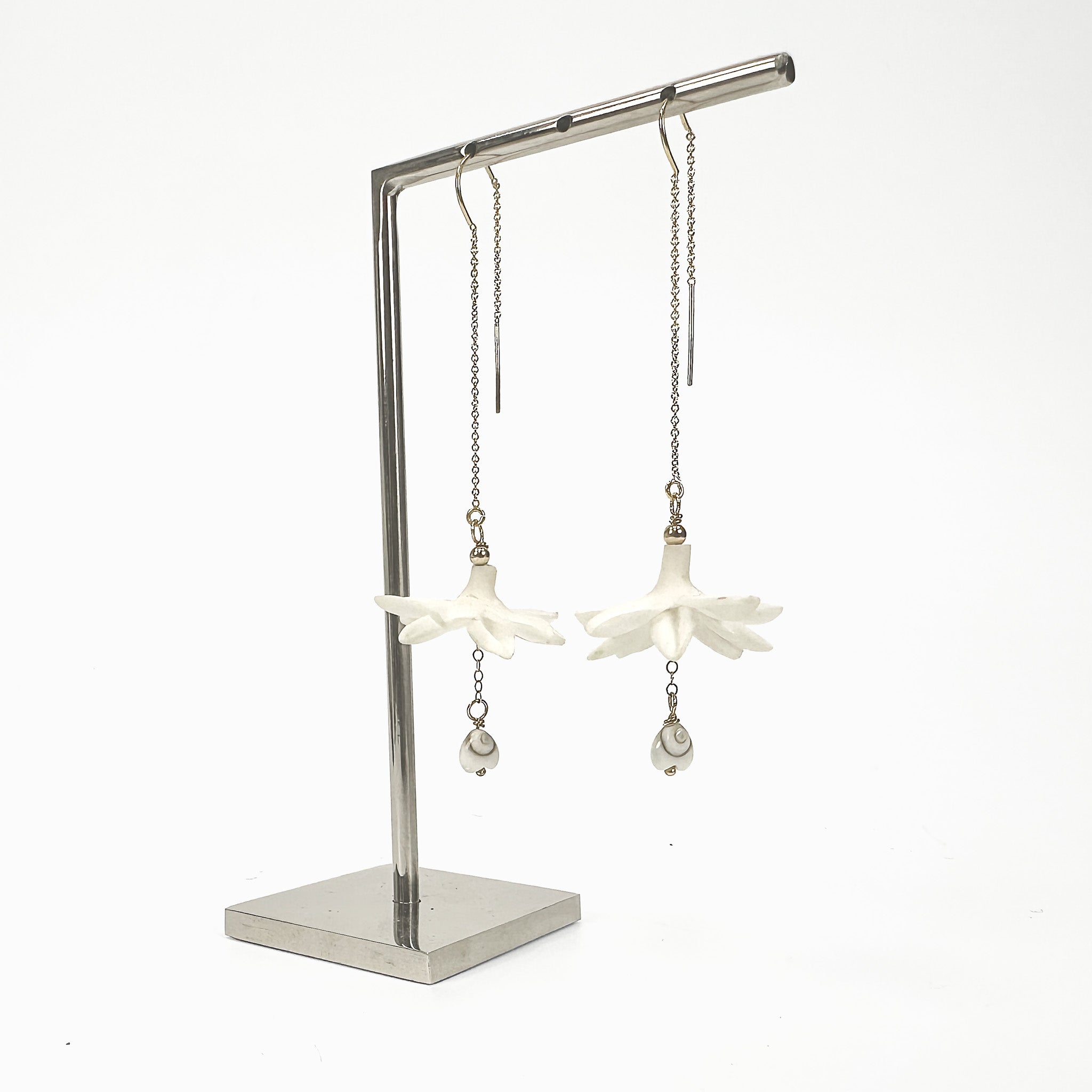 Floating Pikake jasmine earrings with gold-filled threaders and Shiva eye heart drops on a jewelry stand