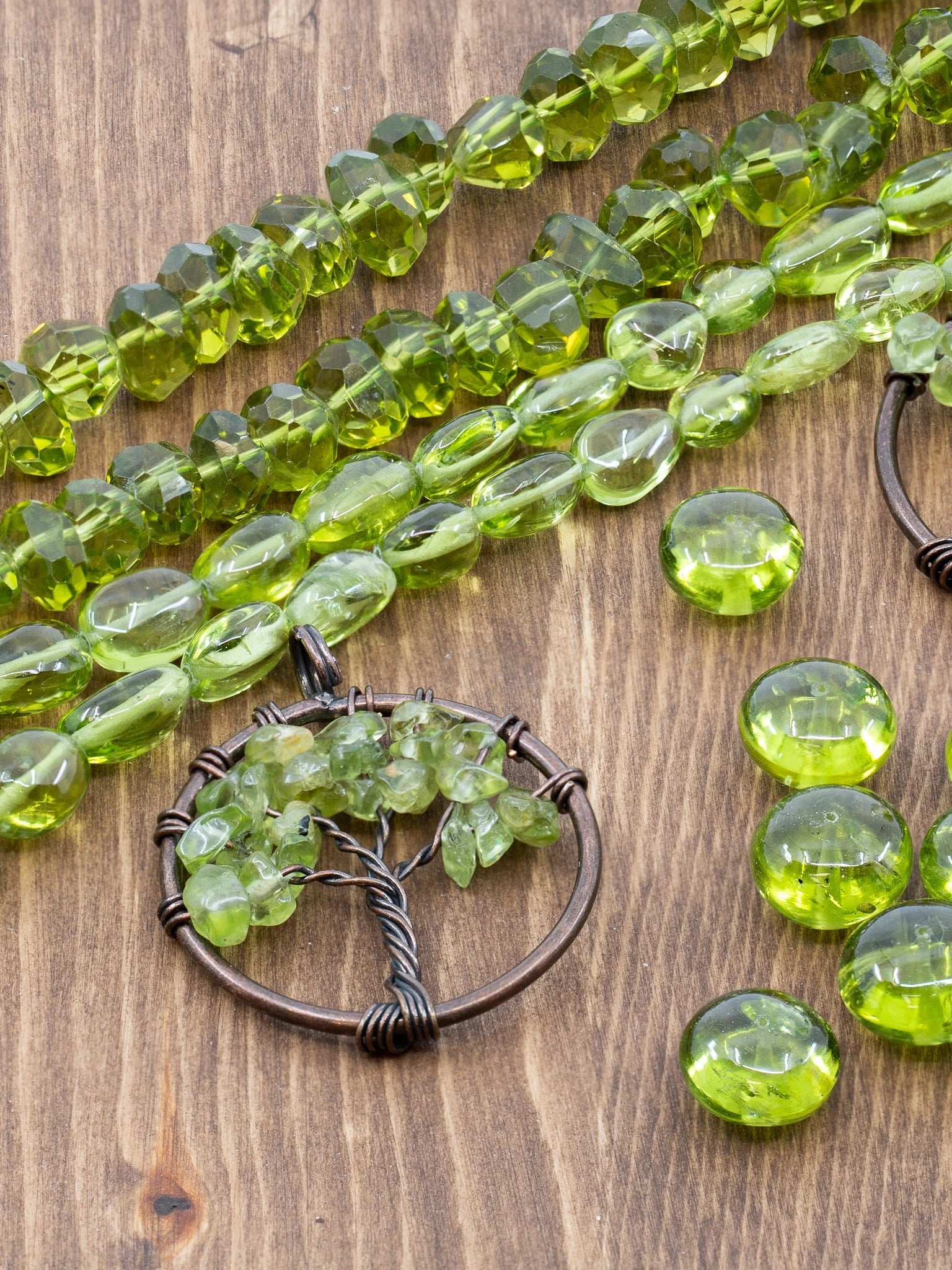 Peridot bead strands, loose Peridot beads, and copper Tree of Life focals on warm wood